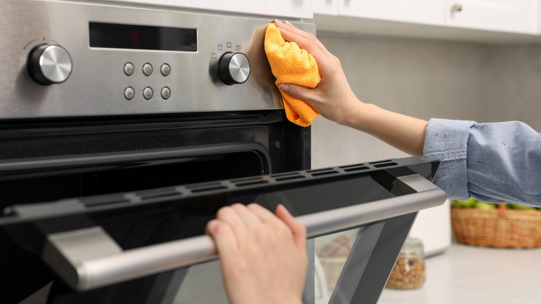 person cleaning oven with towel