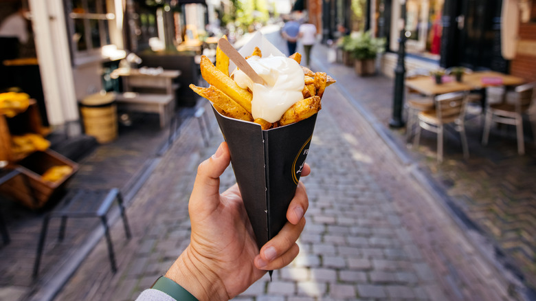 Hand holding cone of Belgian fries topped with mayo