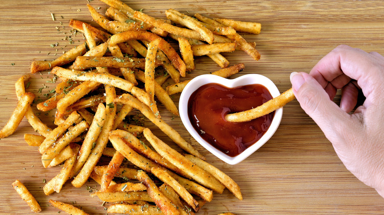 Hand dipping a seasoned French fry into a heart-shaped dish of ketchup