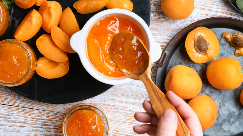 Apricot jam and wooden spoon next two plates of apricots.