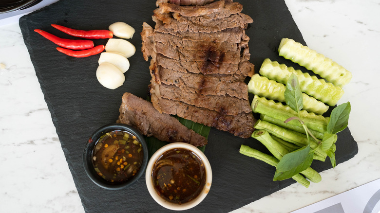 Sliced steak on a black cutting board, next to a dipping bowl of tamarind sauce