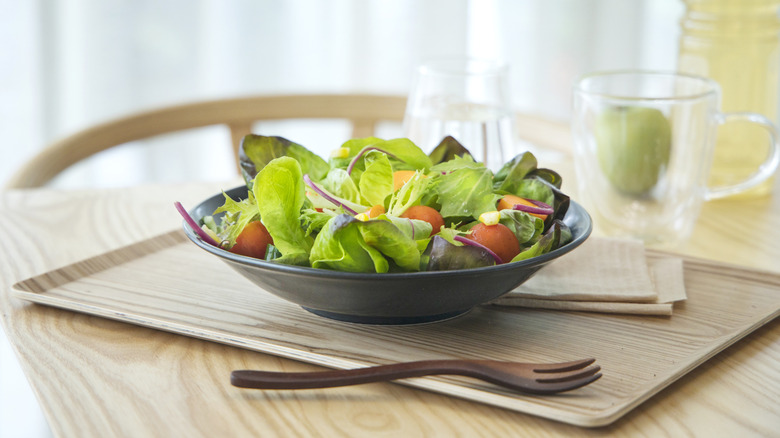 A bowl of salad on a table with a wooden fork and glass mug