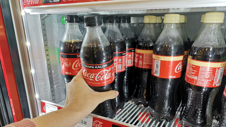 lady grabbing and individually packaged coke out of supermarket fridge