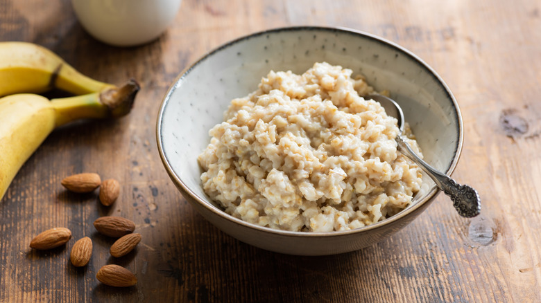 Oatmeal in a white bowl with a metal spoon sitting beside some bananas and almonds