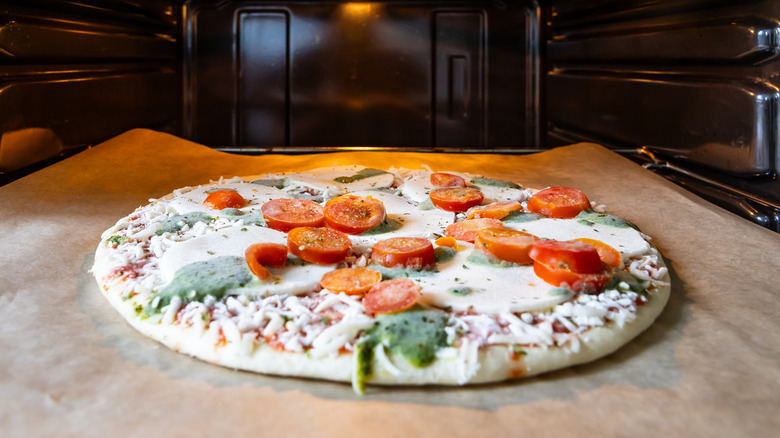 frozen pizza topped with tomatoes going into oven