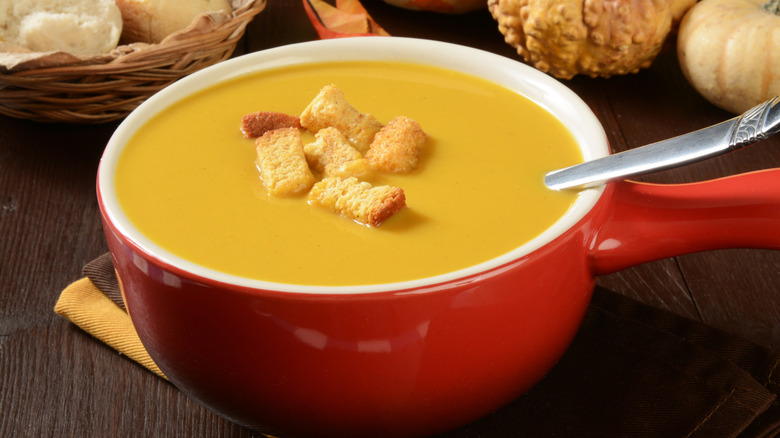 A bowl of soup in a red pot sprinkled with cornbread croutons.