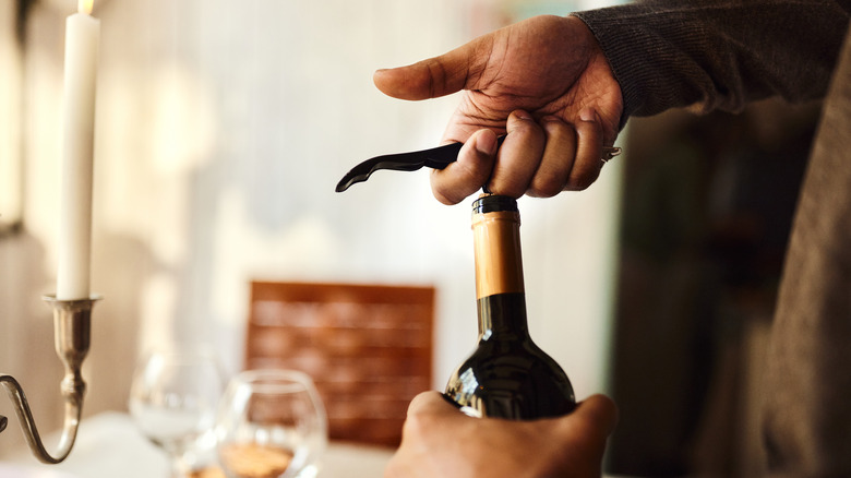 A person opening a bottle of wine with a corkscrew