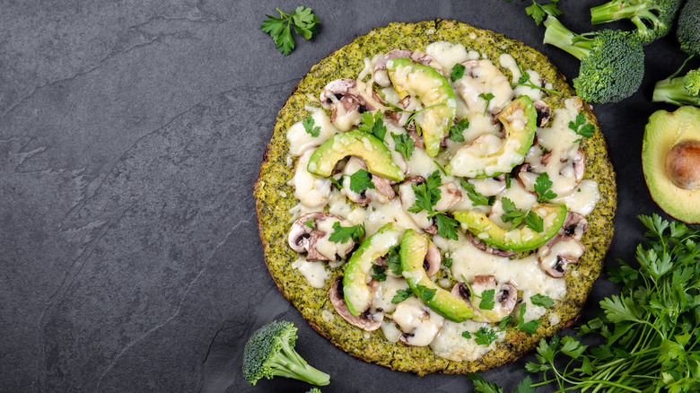 Green broccoli pizza crust topped with avocado, mushrooms, and cream sauce