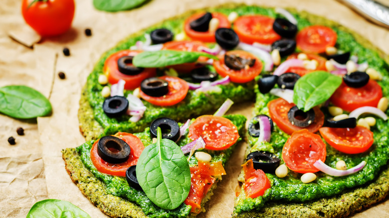 Vegan broccoli pizza topped with spinach pesto, tomatoes, onion, and olives