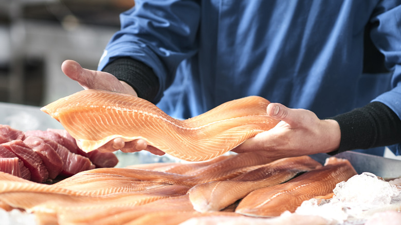 fishmonger holds salmon filet at fish counter at store