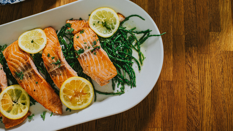 salmon filets sit on a white plate with lemon slices and asparagus