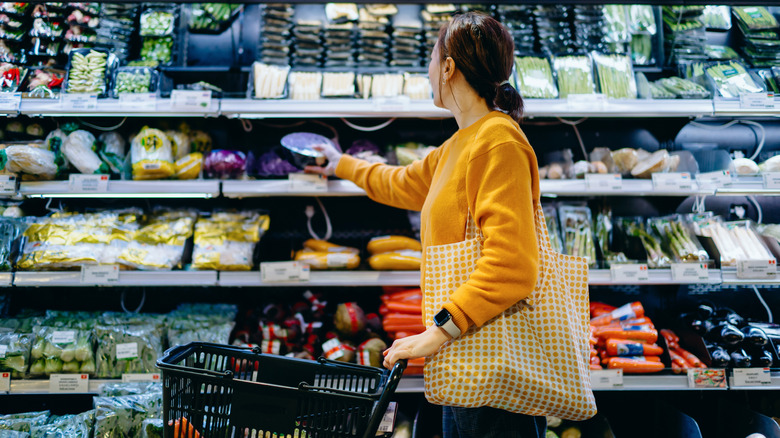 young woman shopping in the grocery store, selecting food from the shelf