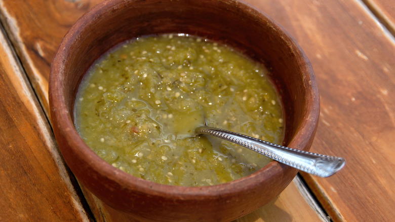 A brown bowl with salsa verde and a spoon in it on a wooden table