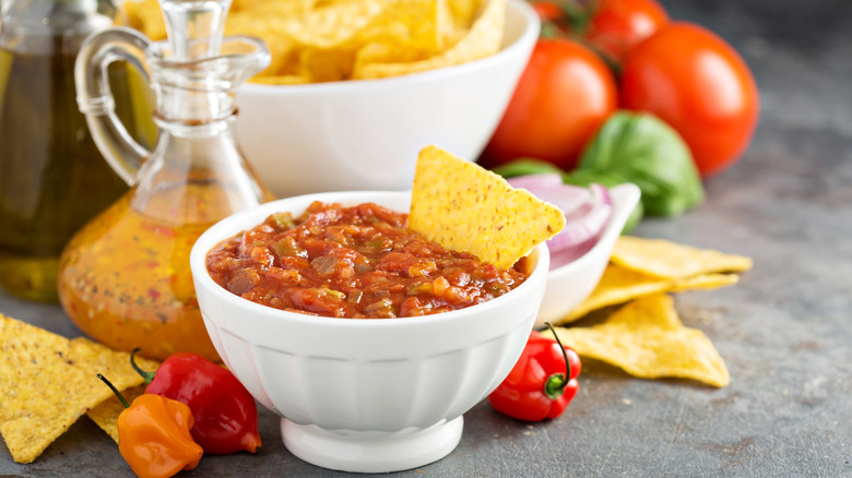 A bowl full of salsa with a tortilla chip sticking out of it