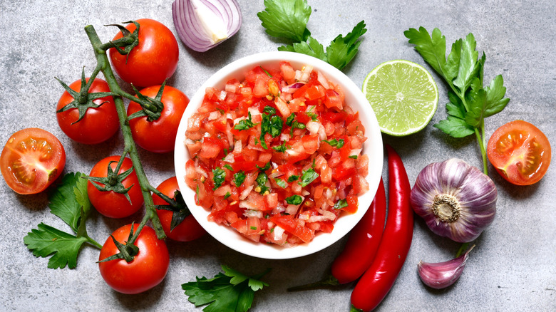 A bowl of chunky salsa surrounded by ingredients