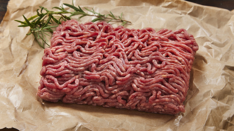 ground beef and a sprig of rosemary on crinkled parchment paper