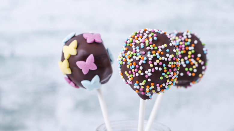 Three chocolate covered cake pops with coroful decoration.