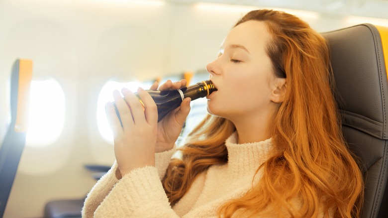 woman drinking from miniature bottle in airplane seat