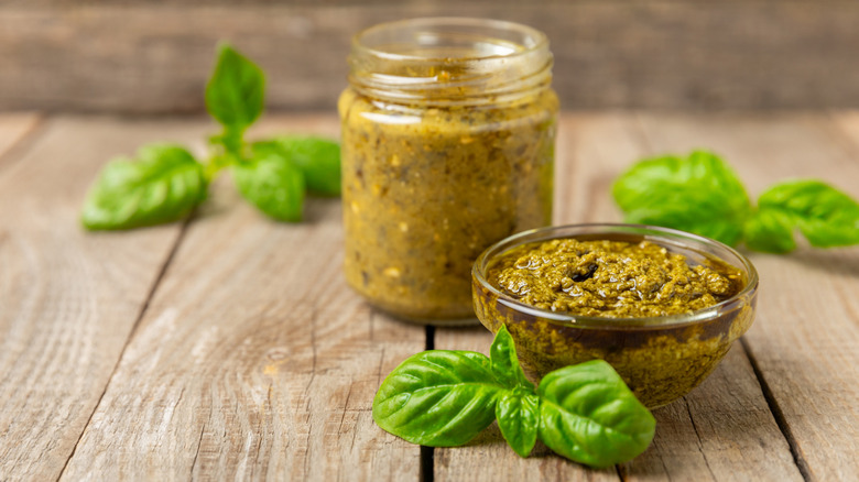 A jar of homemade basil pesto on a wooden counter with sprigs of fresh basil