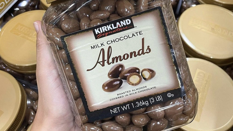 Hand holding container of Kirkland Signature milk chocolate almonds