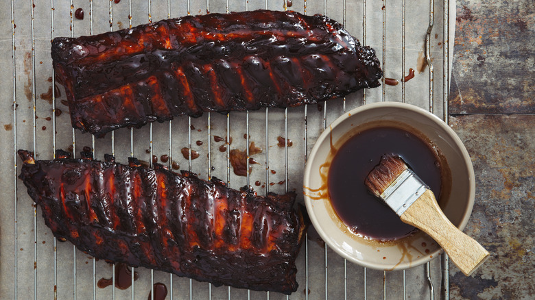 Barbecued ribs on rack next to sauce in bowl