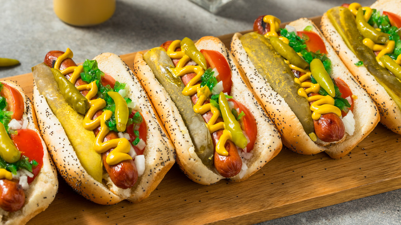 A row of Chicago-style hot dogs topped with mustard and pickles on a wooden board