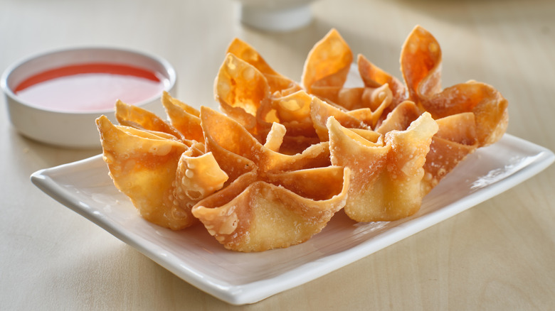 Five pieces of crab rangoon on a rectangular white plate with sweet and sour to the side