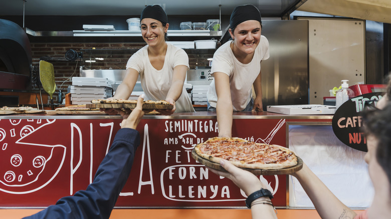 Two people serving pizza out of a food truck window