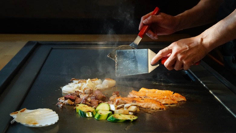 Hands with spatulas over a flat teppan iron grill