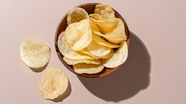 A wooden bowl of potato chips viewed from above.