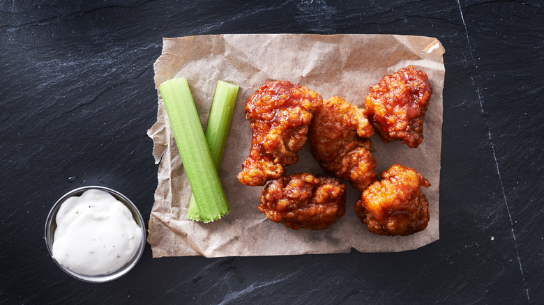 Five boneless wings on parchment paper next to celery sticks and blue cheese dressing