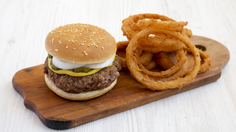 Slugburger accompanied by onion rings on a wooden serving dish.