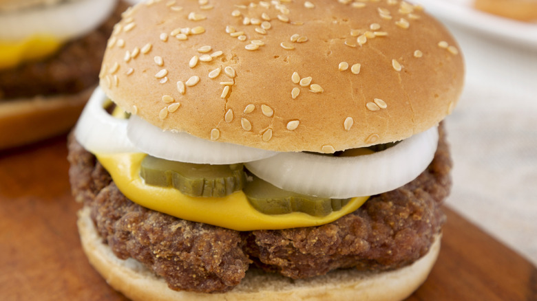 Slugburger on wooden surface with mustard, pickles and onions.