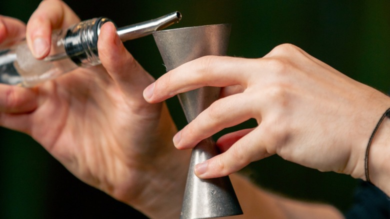 Close-up of bartender using cocktail jigger to measure alcohol.