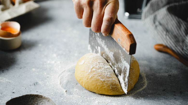 A person dividing pasta dough with a dough cutter.