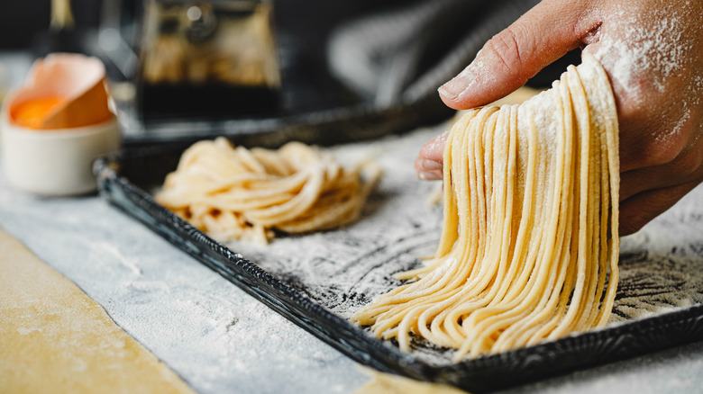 A person putting fresh spaghetti on a tray.