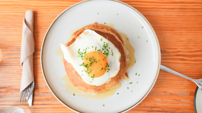 plate of stacked pancakes topped with fried egg garnished with chives