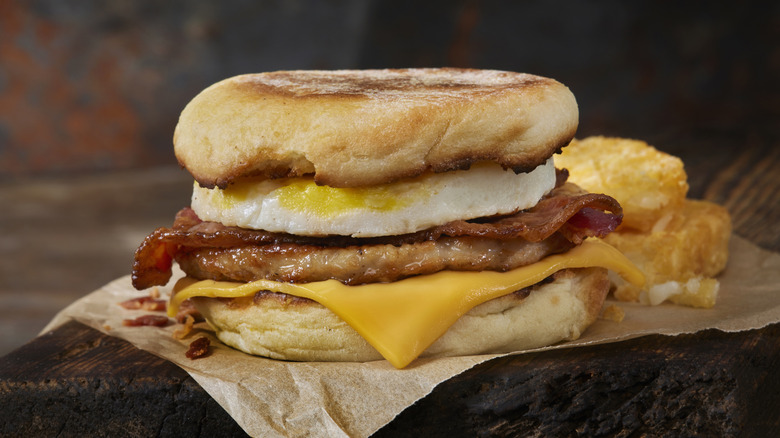 layered breakfast sandwich with english muffins, fried egg, sausage patty and cheese with side of hash browns