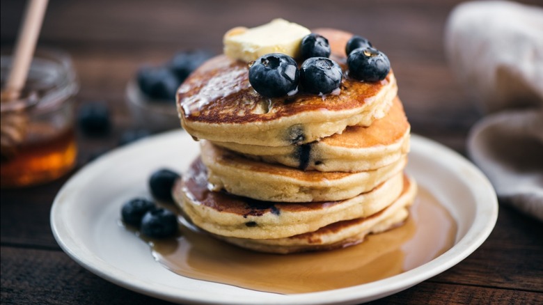 A stack of thick pancakes with blueberries, butter, and syrup