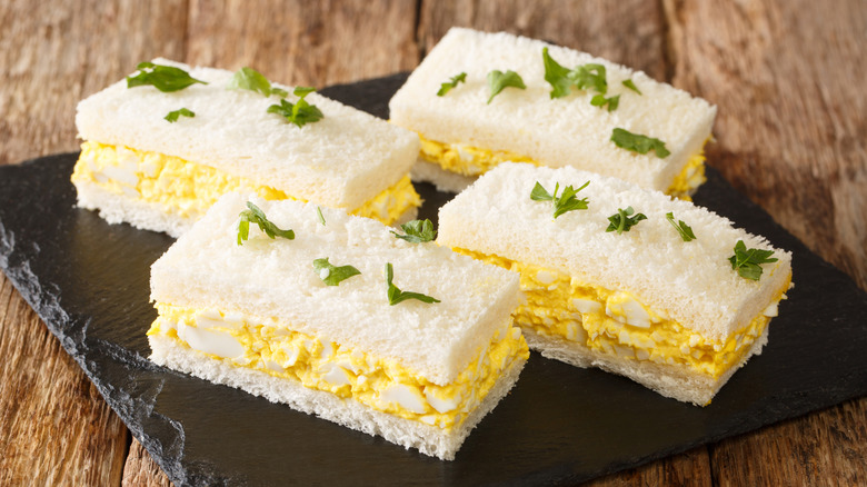 japanese egg salad sandwiches with garnishes on top sit on a black slate