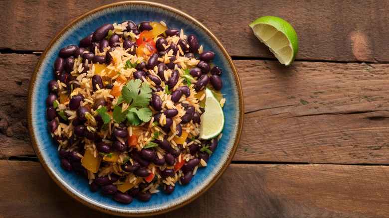 bowl of seasoned rice and beans with tomatoes, peppers, cilantro, and lime over wooden background