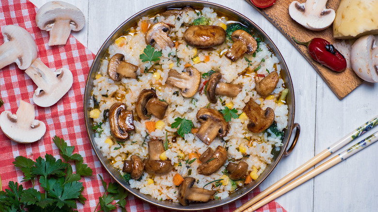 plate of rice, mushrooms, veggies and cilantro beside chopsticks over wooden background