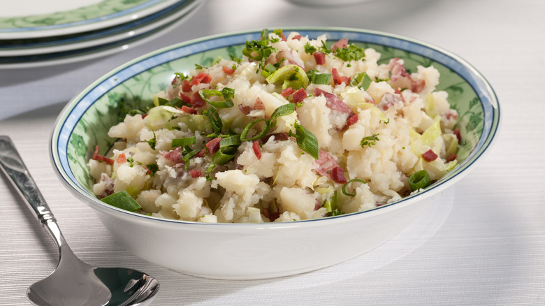 A bowl of mashed potatoes seasoned with cured meat and scallions