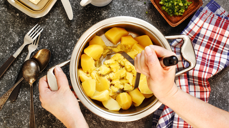 A person mashing potatoes in a pot