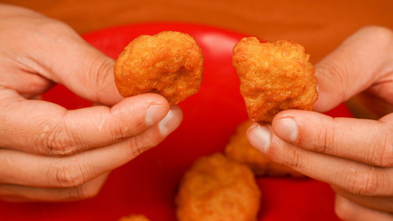 Person holds chicken nuggets in both hands over a red plate with more nuggets