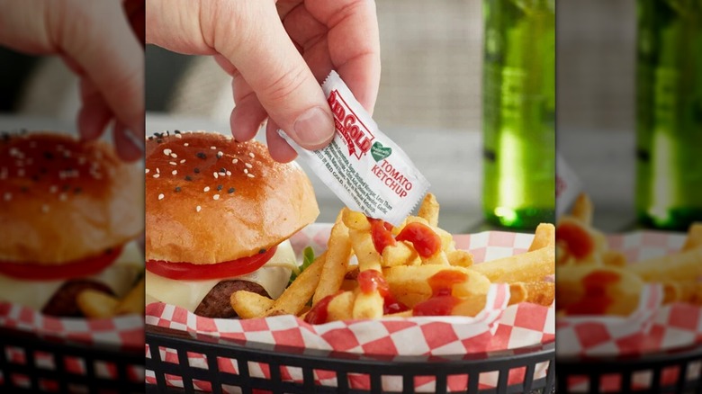 Hand squeezing Red Gold ketchup on fries