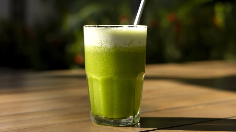 A glass with a green smoothie and metal straw