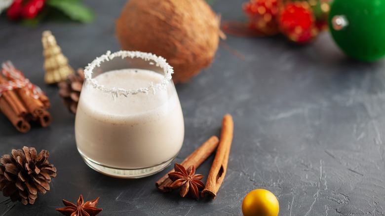 coquito with a whole coconut, Christmas ornaments, and cinnamon sticks