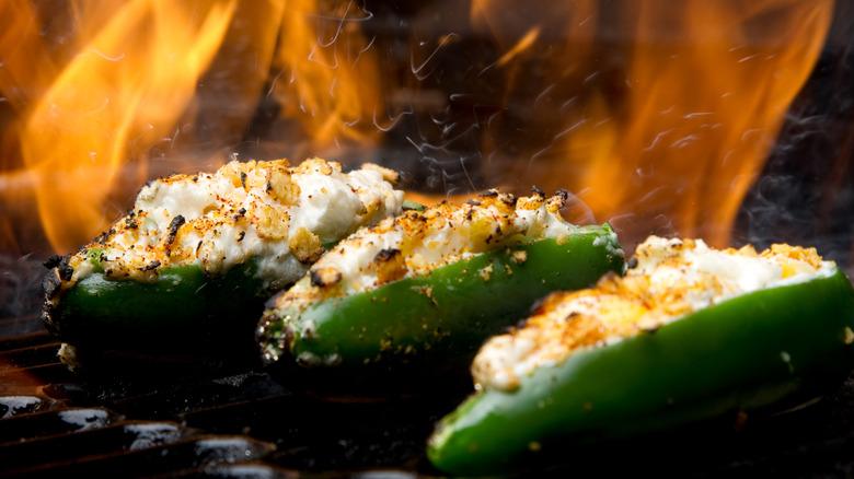 Jalapeño poppers with cheese cooking on a grill with flames