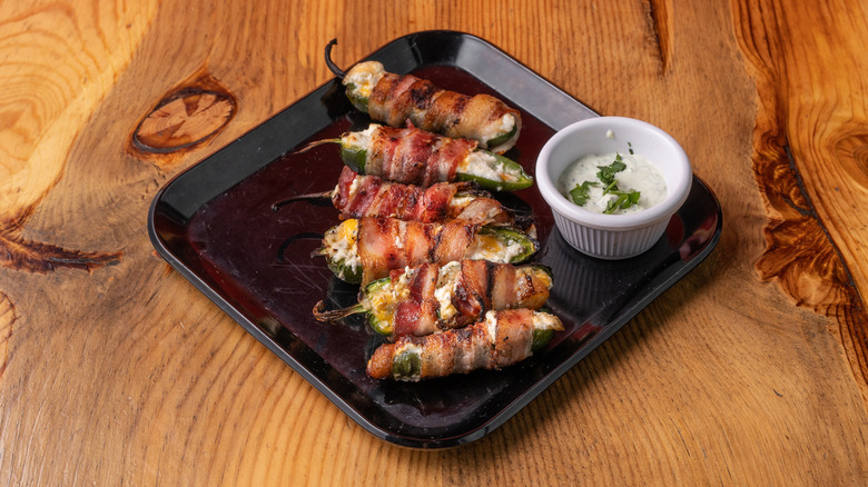 Jalepeño poppers with cream cheese wrapped in bacon on a black plate